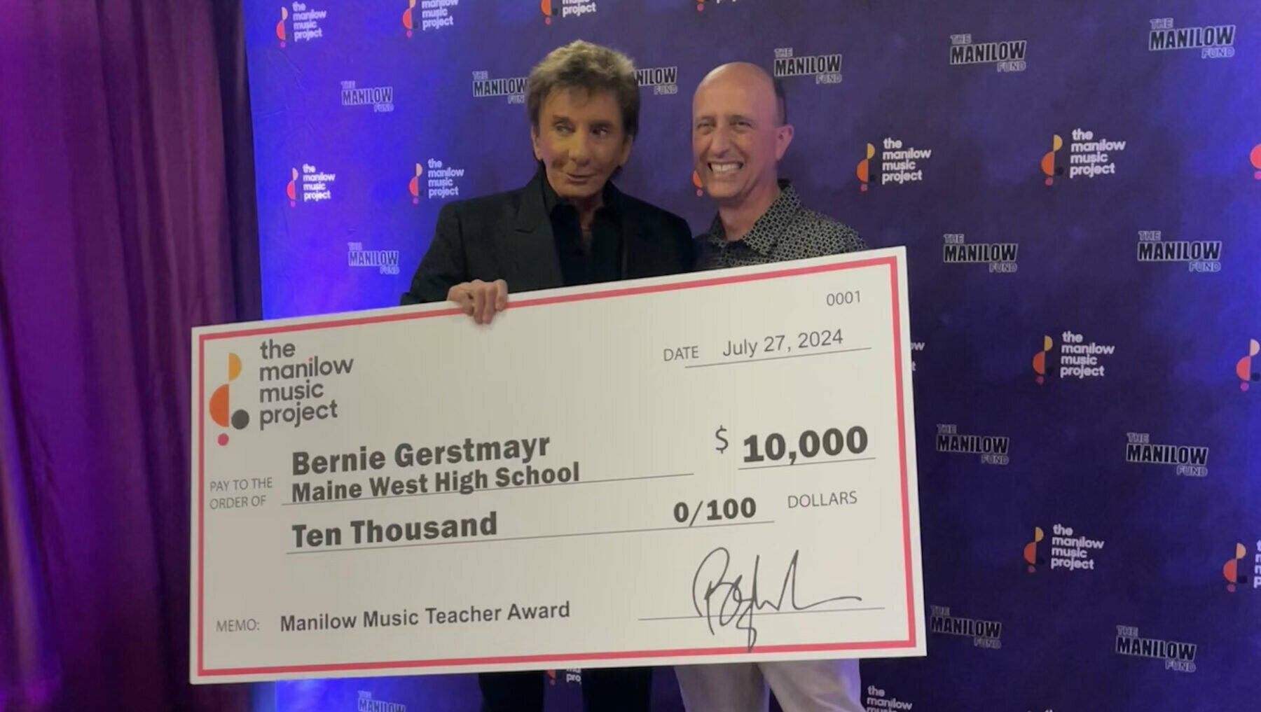 Singer Barry Manilow and teacher Bernie Gerstmayr stand together smiling behind a large ceremonial check for $10,000 from the Manilow Music Project. The check is made out to "Bernie Gerstmayr Maine West High School" for the "Manilow Music Teacher Award," dated July 27, 2024. They are posing in front of a blue backdrop featuring the Manilow Music Project and Manilow Fund logos.