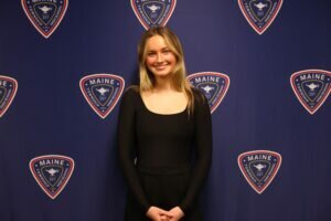 Emma smiling and standing in front of a blue background with D207 logos on it