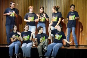 9 students performing during the annual variety show, four sitting on the edge of the stage with five standing behind them.