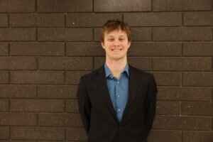 Portrait of Lawson Smiling In Front of a Grey Brick Wall