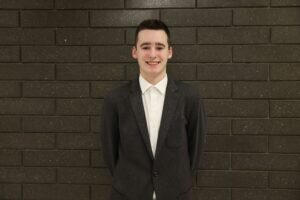 Portrait of Andrew in a Black Suit In Front of a Grey Brick Wall