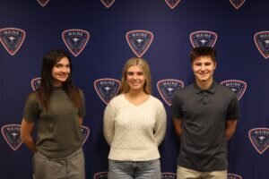 Three students pose in front of a blue background with the District 207 shield logo on it