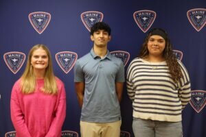 Three students stand in front of a blue Maine Township High School District 207 backdrop.