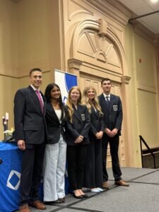 Five students in formal business attire pose together on a stage in front of a DECA banner.