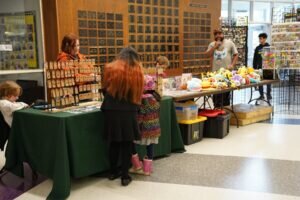 People browse tables covered in small merchandise and plush toys at an indoor craft fair.